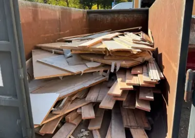 Container mit Holzabfällen, der mit verschiedenen Holzstücken und Platten gefüllt ist, die zur Entsorgung bereitstehen.