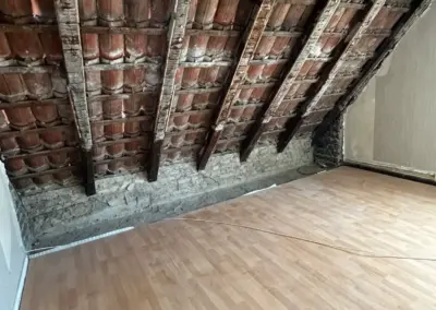 Dachboden mit freiliegenden Holzbalken und einem Holzfußboden, der frisch verlegt wurde. Die Wände sind teilweise verputzt.