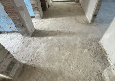 Bodenansicht eines Innenraums mit unebenen, rohen Estrichflächen und sichtbaren Wänden in einem Abbruchprojekt.